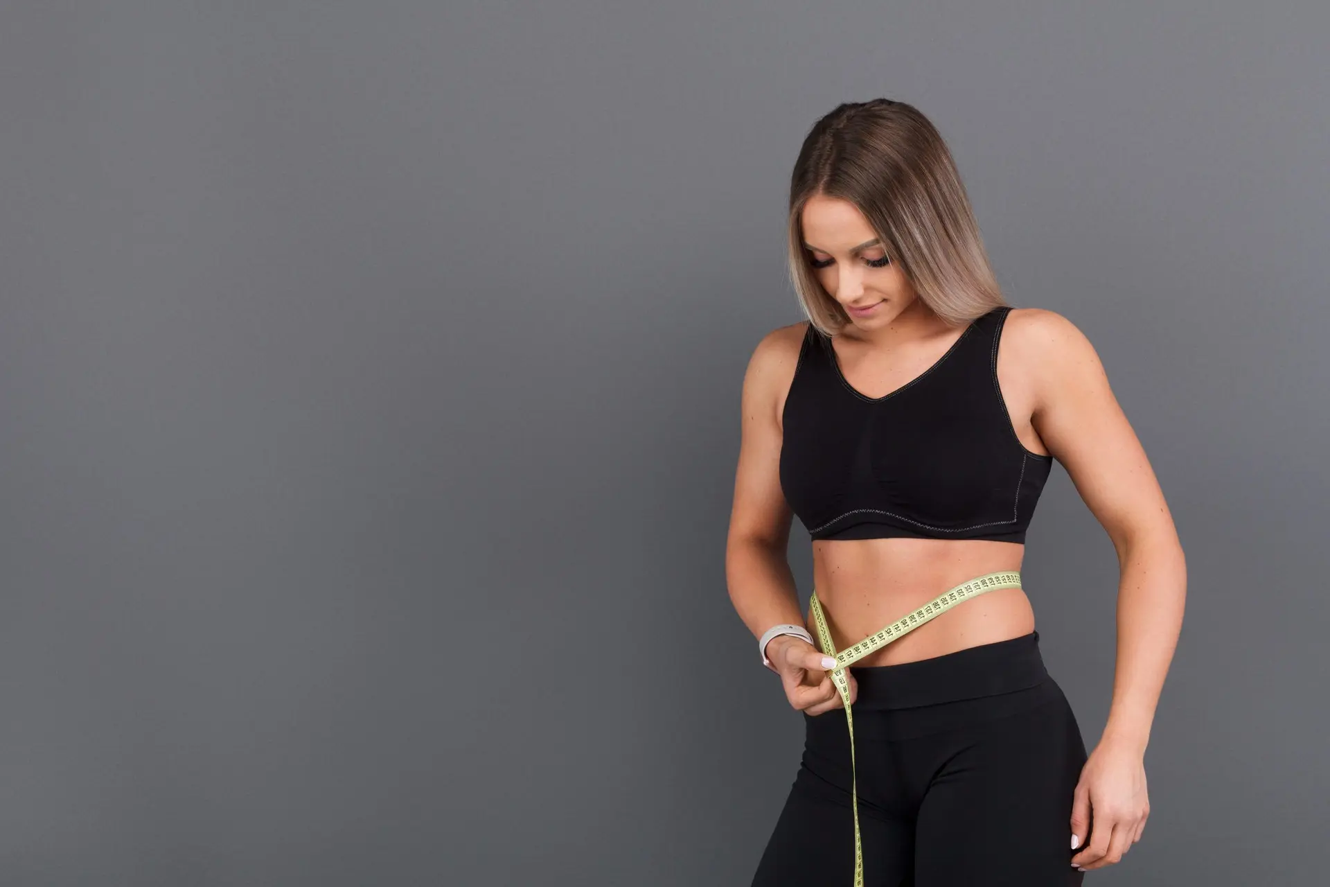Femme en tenue de sport qui mesure son tour de taille avec un mètre ruban