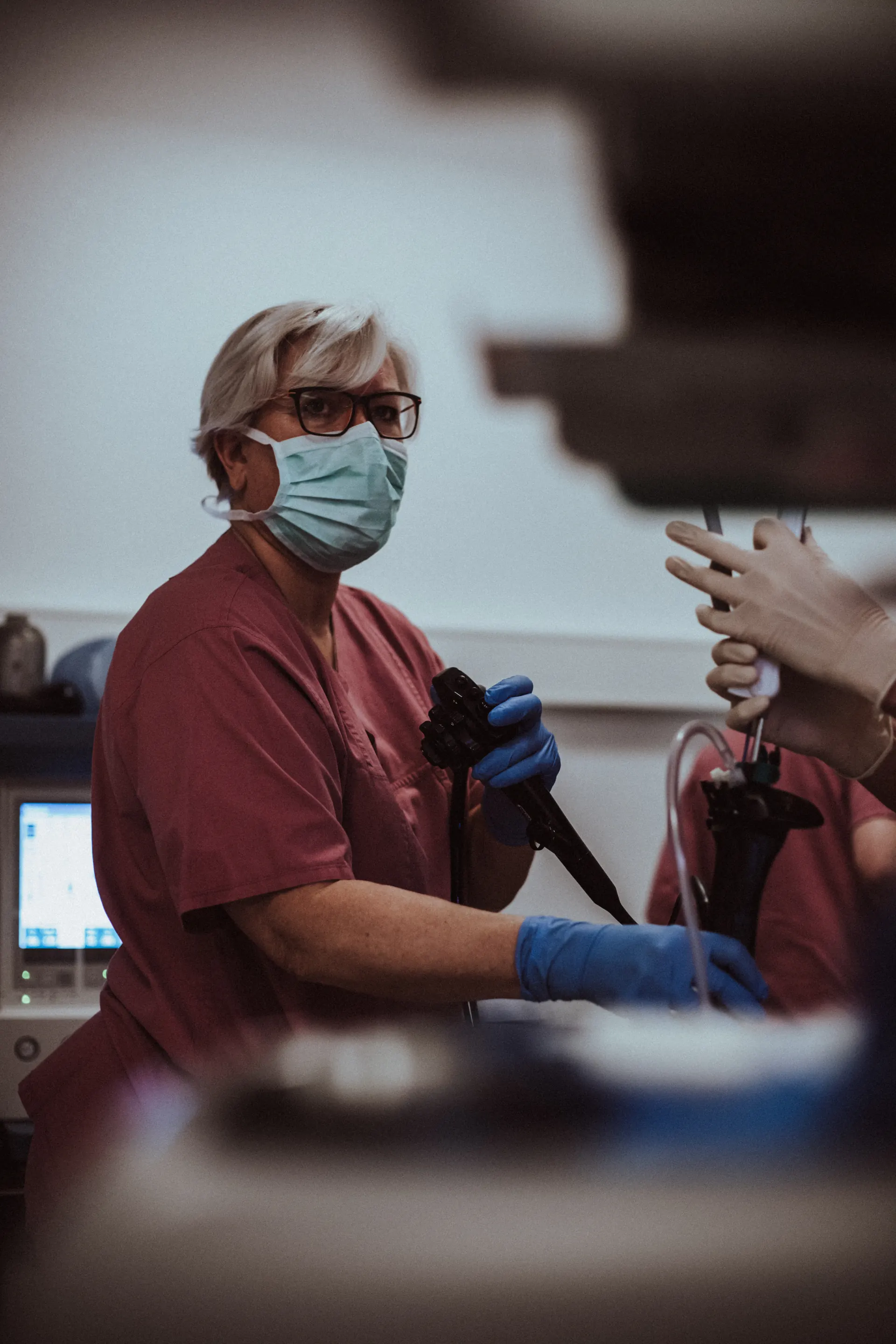 Staff member wearing a mask and gloves holding an endoscope in a treatment room